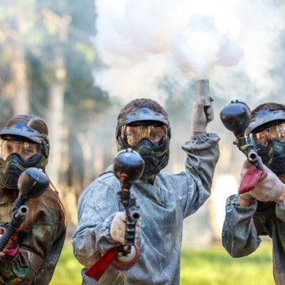 Grupa osób w maskach ochronnych grająca w paintball dla firm.