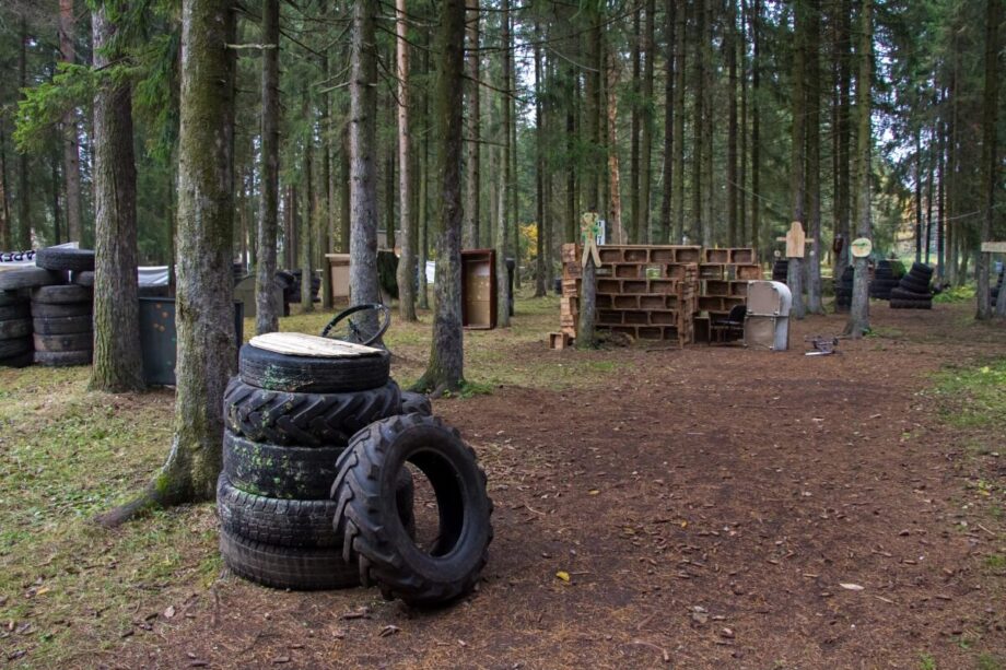 Pole paintballowe w lesie z różnymi przeszkodami wykonanymi z opon i drewnianych struktur.