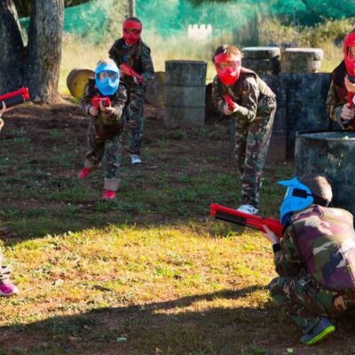 Dzieci bawią się w paintball dla szkół, nosząc kolorowe maski i trzymając broń zabawkową.