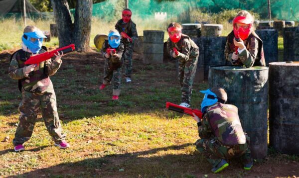 Dzieci bawią się w paintball dla szkół, nosząc kolorowe maski i trzymając broń zabawkową.