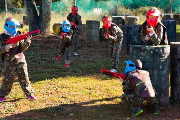 Dzieci bawią się w paintball dla szkół, nosząc kolorowe maski i trzymając broń zabawkową.