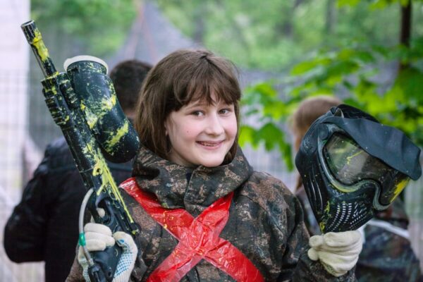 Dziecko trzyma sprzęt na paintball podczas urodzinowej zabawy na świeżym powietrzu.