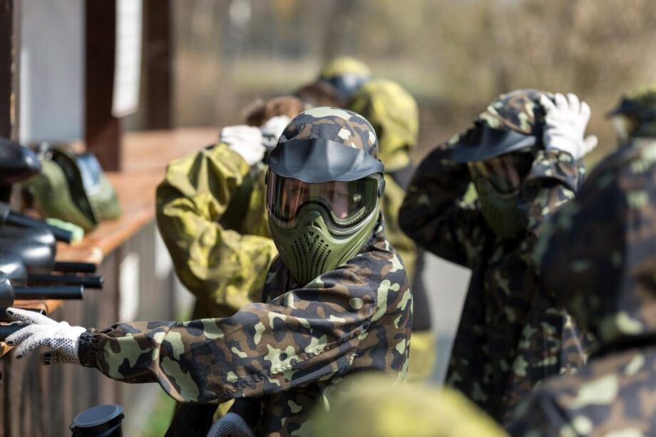 Grupa ludzi w maskach i kombinezonach kamuflażowych przygotowująca się do rozgrywki paintballowej, paintball dla grup zorganizowanych.