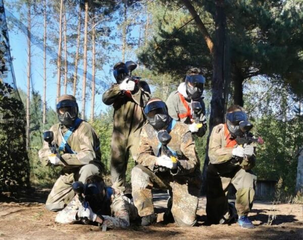 Grupa osób w maskach i kombinezonach gotowa do gry w paintball dla grup zorganizowanych.
